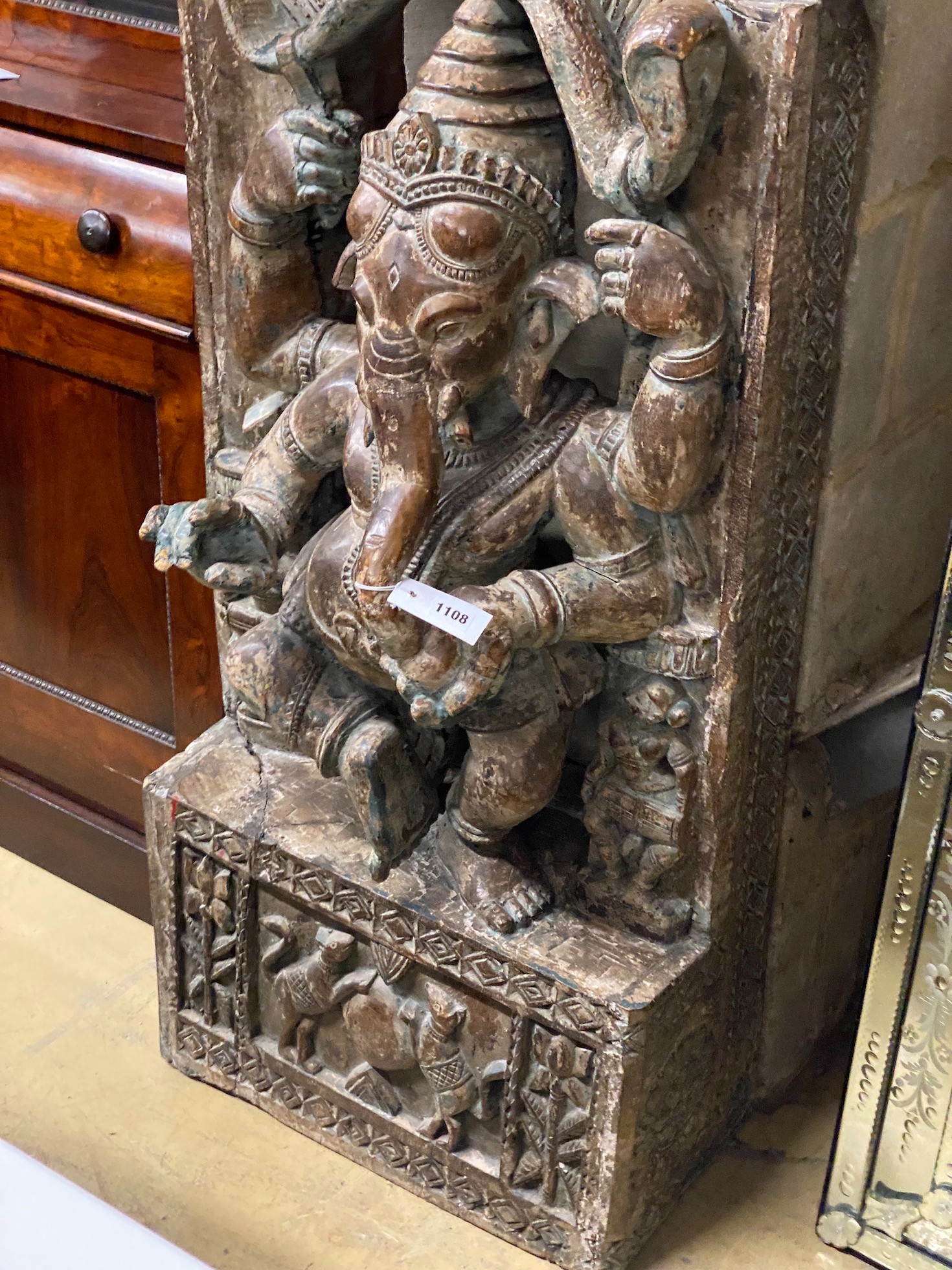 An Indian stained and carved hardwood panel centred with Ganesh, width 54cm, height 160cm
